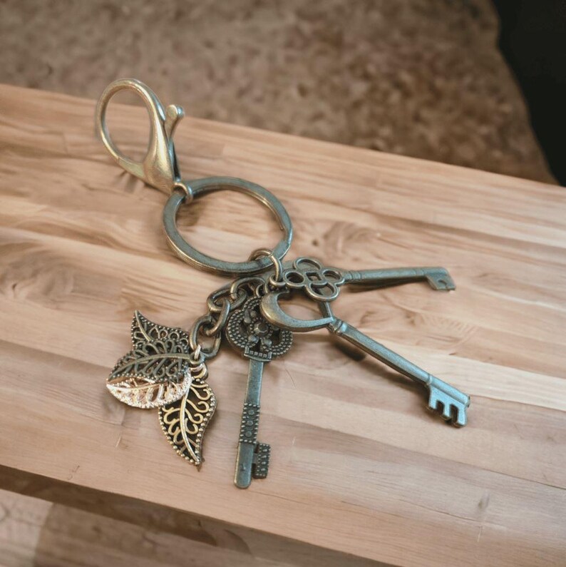 Puede incluir: Un llavero plateado con un dije de hoja decorativa y tres llaves de estilo antiguo. Las llaves tienen dise&ntilde;os intrincados y est&aacute;n unidas a un anillo plateado.