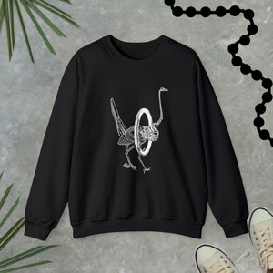 May include: Black sweatshirt featuring a white graphic of a bird with a ring around its neck.