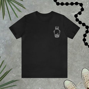 Peut inclure: T-shirt noir avec un motif blanc représentant une bouteille en verre avec un serpent à l'intérieur.