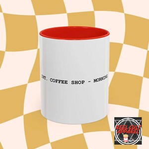 May include: White ceramic coffee mug with a red rim. The mug has black text that reads "INT. COFFEE SHOP - MORNING".
