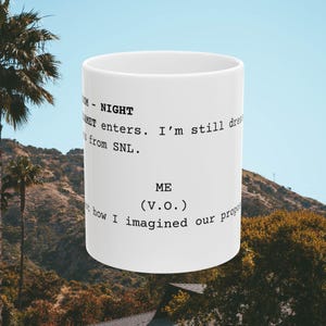 May include: White ceramic mug with a black script design. The text reads "TM - NIGHT WET enters. I'm still dressed from SNL. ME (V.O.) Not how I imagined our proposal."