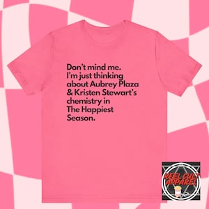 May include: Pink t-shirt with black text that reads "Don't mind me. I'm just thinking about Aubrey Plaza & Kristen Stewart's chemistry in The Happiest Season."