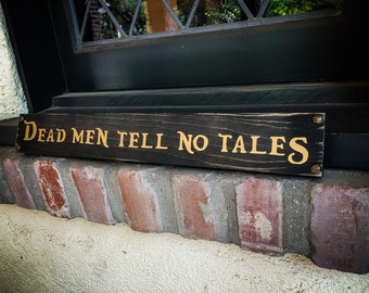 Op de afbeelding: Een zwart houten bord met gouden letters met de tekst "Dead Men Tell No Tales".