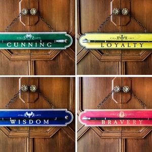 May include: Four wooden signs with black chains hanging from the top. Each sign has a different house crest and a different color. The signs read "Cunning", "Loyalty", "Wisdom", and "Bravery".
