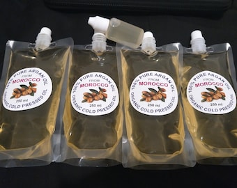 May include: Four clear pouches of 100% pure, organic, cold-pressed argan oil from Morocco. Each pouch contains 250 ml of oil and has a white label with text and an illustration of argan nuts. A small dropper bottle is also present.
