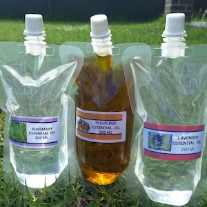 Peut inclure: Trois sachets d'huiles essentielles avec un bec verseur blanc et une étiquette. Les étiquettes indiquent "Rosemary Essential Oil 200 ml", "Clove Bud Essential Oil 200 ml" et "Lavender Essential Oil 200 ml". Les huiles sont claires et ambrées.