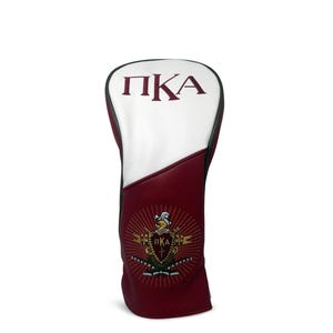 May include: A maroon and white golf club head cover. The top portion is white with maroon Greek letters. The bottom portion is maroon with a gold emblem. The cover is designed to protect golf clubs.