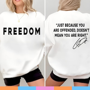 May include: White sweatshirt with the word "FREEDOM" printed in large, black letters on the front. The back of the sweatshirt features the quote, "JUST BECAUSE YOU ARE OFFENDED, DOESN'T MEAN YOU ARE RIGHT." in black.