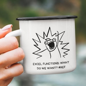 Pode incluir: Caneca esmaltada branca com borda e alça pretas. A caneca apresenta um gráfico de desenho animado em preto e branco e o texto "EXCEL FUNCTIONS: WHAT DO WE WANT? #REF". A caneca é segurada por uma pessoa.