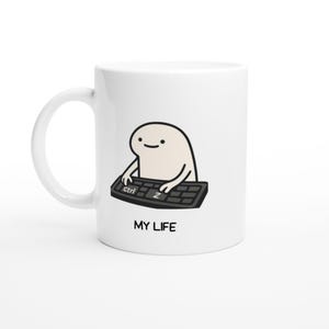Puede incluir: Taza de cerámica blanca con un personaje de dibujos animados escribiendo en un teclado negro. El personaje beige tiene una cara sencilla. El texto "MY LIFE" está impreso debajo del teclado. La taza tiene un asa curva.
