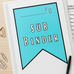 May include: A white binder with a teal banner reading "SUB BINDER" in bold, black letters. The banner has a black border and a line above "SUB". A black pen and paperclips are visible.