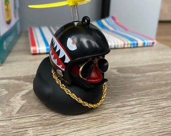 May include: Black rubber duck with a black helmet with a shark tooth design, red and black sunglasses, and a gold chain. The duck has a yellow propeller on top of the helmet.