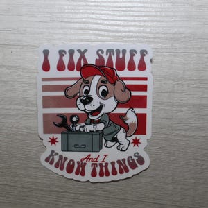 May include: A white sticker with a cartoon dog wearing a red hat and holding a toolbox. The text on the sticker reads "I fix stuff and I know things".