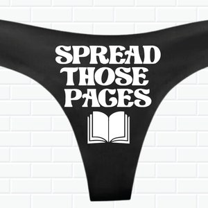 May include: Black thong underwear with white text that reads "SPREAD THOSE PAGES" and a white outline of an open book.