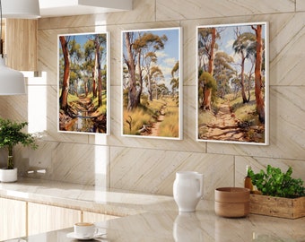 May include: Three framed landscape paintings of Australian bush scenes with trees and dirt paths. The paintings are in white frames and are hung on a beige tiled wall.