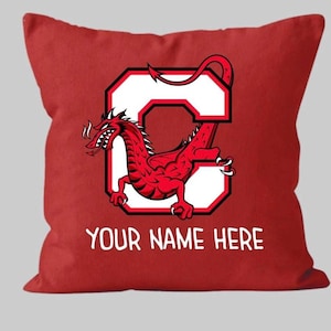 May include: Three decorative throw pillows with a red dragon and a white letter C on a black, white, and red background. The red pillow has the text "Your Name Here" printed on it.