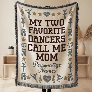 May include: A beige throw blanket with a dark brown fringe. The blanket features the text "MY TWO FAVORITE DANCERS CALL ME MOM" in dark brown, with ballet-themed graphics and the word "Personalize Names" in a script font.