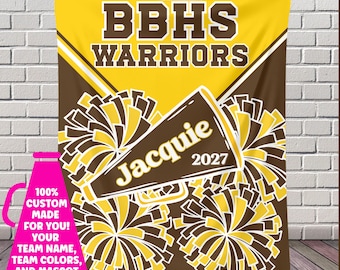 May include: A yellow and brown custom blanket with the text "BBHS WARRIORS" and "Jacquie 2027". The blanket features a megaphone and pom-pom design. A pink graphic on the left says "100% CUSTOM MADE FOR YOU! YOUR TEAM NAME, TEAM COLORS, AND MASCOT".