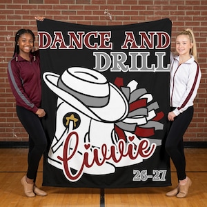 May include: A black fleece blanket featuring the text DANCE AND DRILL in white and maroon, a white cowboy hat, a white boot with a star, maroon and gray pom-poms, the name Livvie in maroon script, and the text 26-27 in white at the bottom.