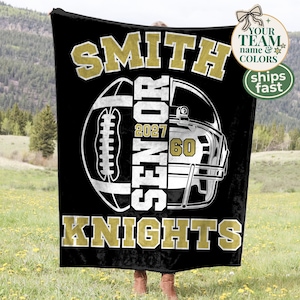 May include: A black fleece blanket featuring a large white and gold graphic of a football and a helmet. The text reads SMITH, SENIOR, 2027, 60, and KNIGHTS in bold block lettering. The design is centred on the fabric with high-contrast colours.