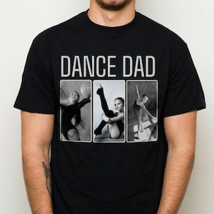 Op de afbeelding: Zwart t-shirt met de tekst "DANCE DAD" in witte blokletters. Het shirt heeft drie zwart-wit afbeeldingen van jonge dansers in verschillende poses. De dansers dragen turnpakjes en panty's.