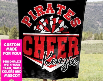 May include: Black blanket with the words "PIRATES CHEER Kenzie" in red and white. The blanket has a pom-pom design and a pink banner that says "CUSTOM MADE FOR YOU! PERSONALIZE WITH YOUR TEAM, NAME, COLORS AND MASCOT."