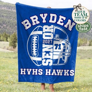 May include: A royal blue fleece blanket featuring a white graphic of a football helmet and a football. The text reads BRYDEN, SENIOR, 2027, 71, and HYHS HAWKS in bold white lettering. The design is centred on the fabric with a soft texture.