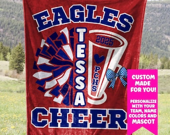 May include: Red fleece blanket with a cheerleading design. The blanket features a blue and white pom-pom, a megaphone with the text "PCHS" and "2025", and the words "EAGLES TESSA CHEER".