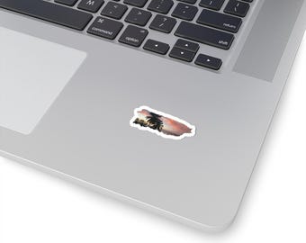 May include: A rectangular sticker depicting a tropical sunset with palm trees silhouetted against a pink and orange sky. The sticker is on a silver laptop.