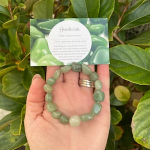May include: A green aventurine gemstone bracelet with a card that reads "Aventurine Origin: various locations Colour: green, blue, red, brown, peach Aventurine is a very positive stone of prosperity. This crystal defuses negative situations and turns them around. Wearing Aventurine absorbs electromagnetic smog and protects against environmental pollutants."