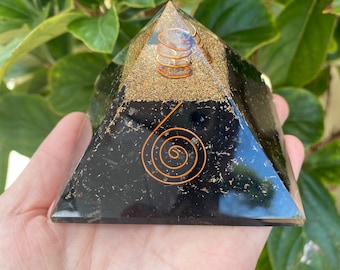 May include: Black obsidian pyramid with a copper wire spiral design. The pyramid is layered with clear quartz crystals and gold flakes.