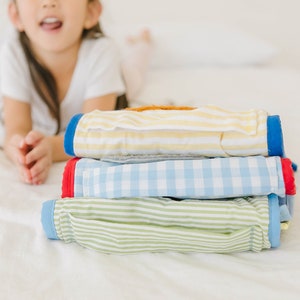 May include: A stack of four folded baby clothes in different patterns. The top layer is yellow and white striped, the second layer is blue and white checkered, the third layer is green and white striped, and the bottom layer is blue and white striped.