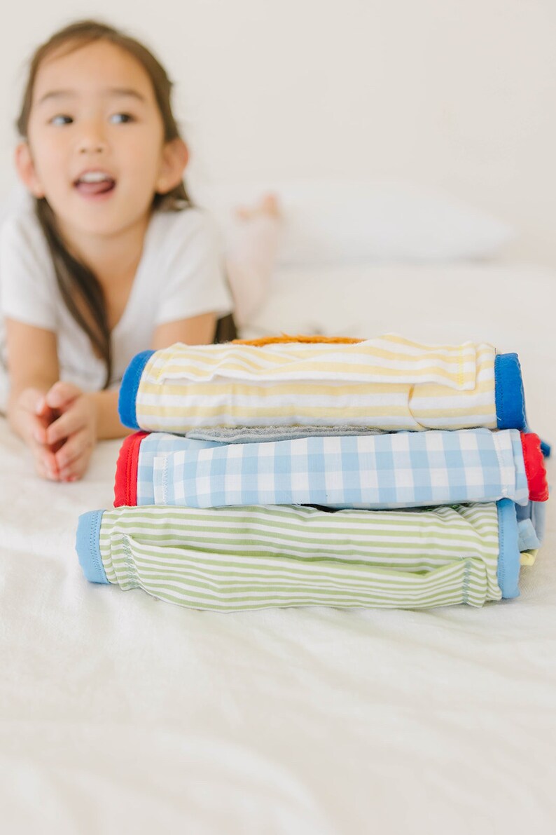 May include: A stack of four folded baby clothes in different patterns. The top layer is yellow and white striped, the second layer is blue and white checkered, the third layer is green and white striped, and the bottom layer is blue and white striped.