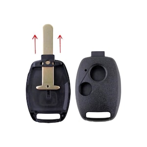 May include: Two black plastic key fob shells for a car key. The shell on the left is open, revealing a gold metal key blade. The shell on the right is closed and has three buttons.