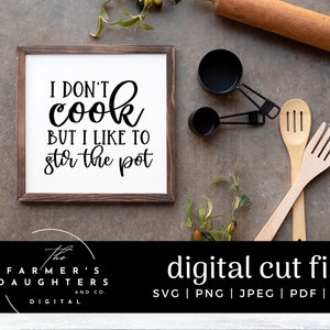 Puede incluir: Un letrero de madera marrón con texto blanco que dice "No cocino pero me gusta remover la olla". El letrero está sobre un fondo rústico con utensilios de cocina y vegetación.