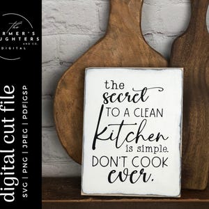 Op de afbeelding: Een wit houten bord met zwarte tekst die luidt: "Het geheim van een schone keuken is simpel. Kook nooit."