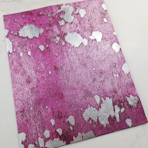 May include: A sheet of pink and silver faux leather with a speckled pattern. The silver is in a splatter pattern.