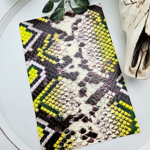 May include: A close-up of a yellow, black, and white snakeskin pattern. The pattern is printed on a flat surface, possibly a piece of fabric or paper.