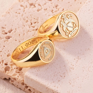 May include: Two gold signet rings with engraved details. One ring features a crest with the name Sainsbury and the interior name Leon. The other ring displays a triangular emblem with the text Cavalier della Liberta 55 Milano and the date 20.11.2025.