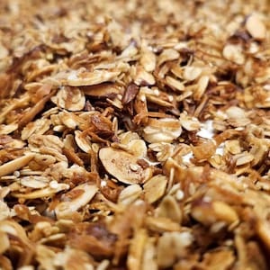 Pode incluir: Close-up de um lote de granola caseira com aveia torrada, amêndoas e uma cor marrom clara.