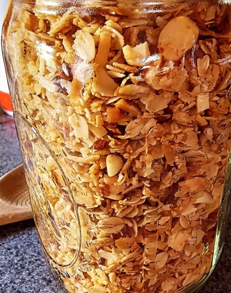 Pu&ograve; includere: Un barattolo di vetro pieno di granola fatta in casa. La granola &egrave; un mix di fiocchi d'avena, scaglie di cocco, noci e frutta secca. La granola &egrave; di colore marrone chiaro e ha una consistenza leggermente croccante.