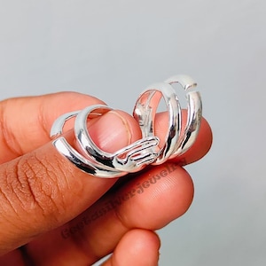 Könnte beinhalten: Zwei silberne Ringe, die miteinander verschlungen sind und ein Paar Hände bilden, die sich halten. Die Ringe sind offen und können an jedem Finger getragen werden.