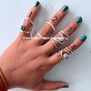 以下が含まれることがあります： 手には4つのシルバーリングがあり、それぞれユニークなデザインです。1つのリングにはターコイズストーンがあり、他のリングにはテクスチャまたは幾何学模様があります。リングは1から4まで番号が付けられており、さまざまなスタイルを示しています。