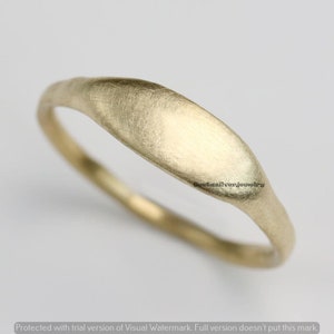 Könnte beinhalten: Ein schlichter, gebürsteter Goldring mit leicht abgerundeter, flacher Oberseite. Der Ring ist aus glattem, mattem Metall gefertigt.