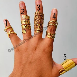 May include: Five gold-toned rings, each with a unique design, are worn on a hand. The rings are numbered 1 through 5.