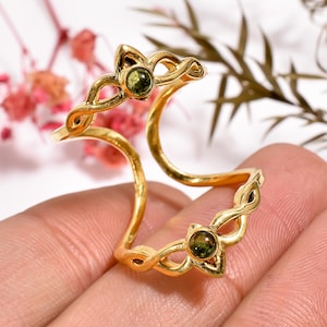 Peut inclure: Bague en or avec un motif de nœud celtique et deux pierres précieuses vertes. La bague est ouverte et réglable.