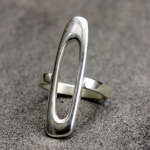 May include: A silver ring with a unique oval-shaped design. The ring is made of a single piece of metal, with a large oval cutout in the center.
