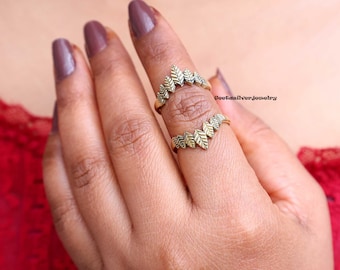 Op de afbeelding: Een ring in bladvorm van goudkleur met een gesplitst ontwerp, gedragen aan een vinger. De ring bestaat uit twee aparte delen die in elkaar passen.