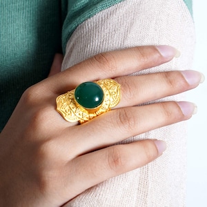 Könnte beinhalten: Ein goldener Ring mit einem verzierten Design und einem großen, runden, grünen Edelstein.