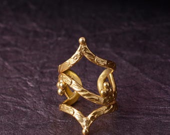 May include: A gold-toned ring featuring an open, multi-layered design with a textured surface. The band consists of two V-shaped segments connected by curved elements, accented with small spherical beads at the terminals and junctions.